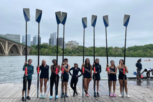 Girls crew team holding oars on a dock.