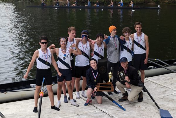 Boys rowing team posing on dock with trophy.